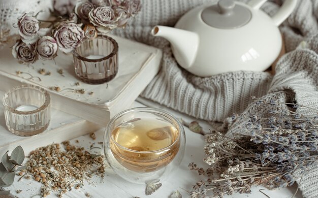 Cozy light still life with candles, a cup of tea, a teapot and dry herbs.