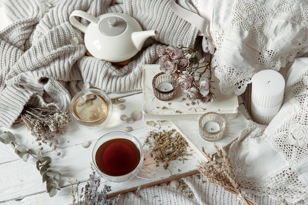 Cozy light still life with candles, cups of tea, teapot and flowers as decor.