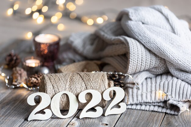 Cozy New Year's composition with decorative numbers 2022, knitted elements and bokeh lights.