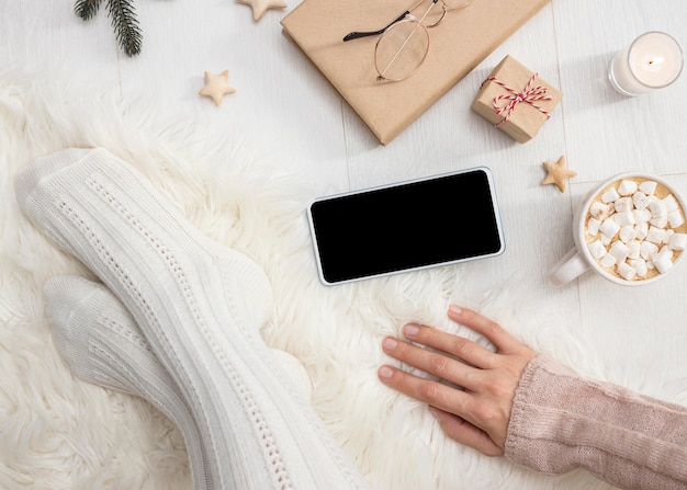 Cozy person at home with smartphone and cup of hot cocoa with marshmallows