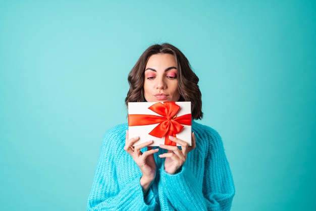 Cozy portrait of a young woman in a knitted blue sweater and bright pink makeup holding a gift box
