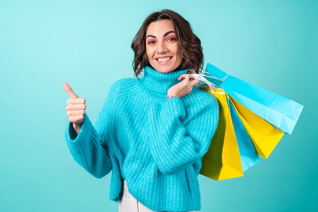 ショッピングバッグを保持しているターコイズブルーのニットの青いセーターと明るいピンクのメイクで若い女性の居心地の良い肖像画