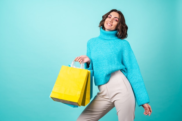 Cozy portrait of a young woman in a knitted blue sweater and bright pink makeup on turquoise holding shopping bags