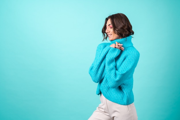 Cozy portrait of a young woman in a knitted blue sweater and bright pink makeup on turquoise