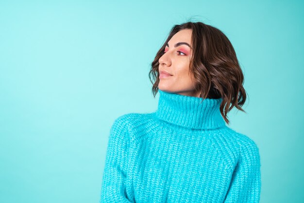 Cozy portrait of a young woman in a knitted blue sweater and bright pink makeup on turquoise