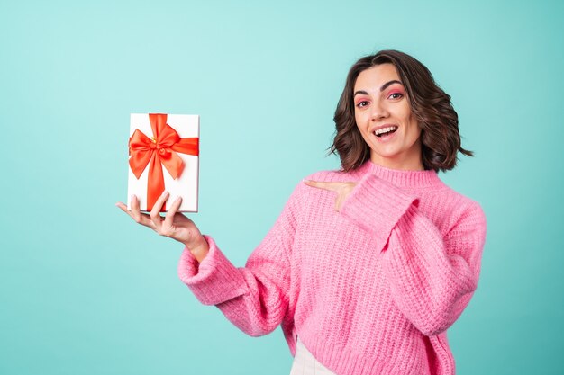 Cozy portrait of a young woman in a pink knitted sweater and with bright makeup on turquoise with a gift box with a red bow