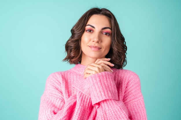 Cozy portrait of a young woman in a pink knitted sweater and with bright makeup on turquoise