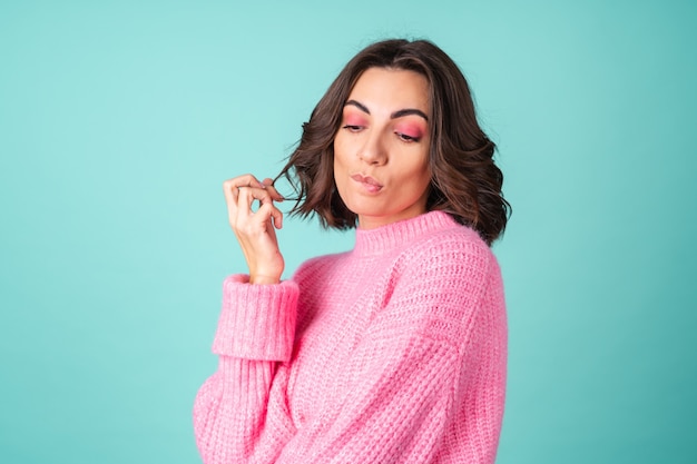 Cozy portrait of a young woman in a pink knitted sweater and with bright makeup on turquoise