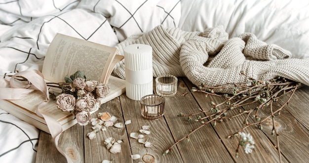 Free photo cozy spring still life with candles, knitted element, book and flowers.