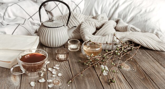 Cozy spring still life with candles, tea, kettle on a wooden surface in a rustic style.