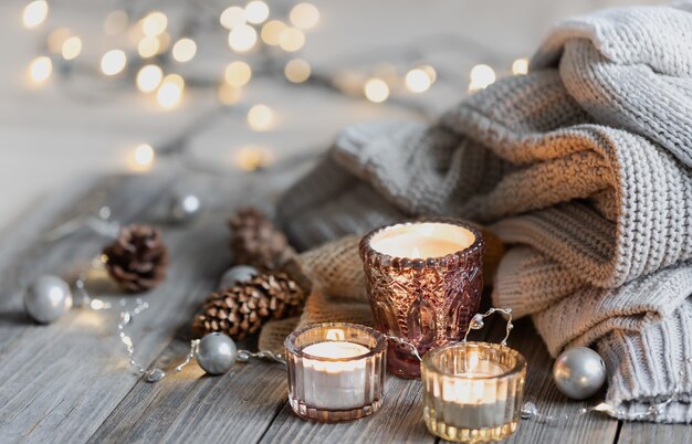 Cozy winter background with burning candles, decorative details, knitted elements with bokeh lights, copy space.