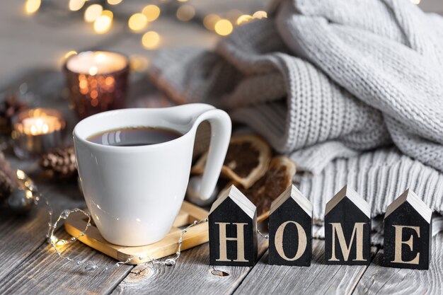 Cozy winter composition with a cup of tea, the decorative word home, knitted elements and bokeh lights.