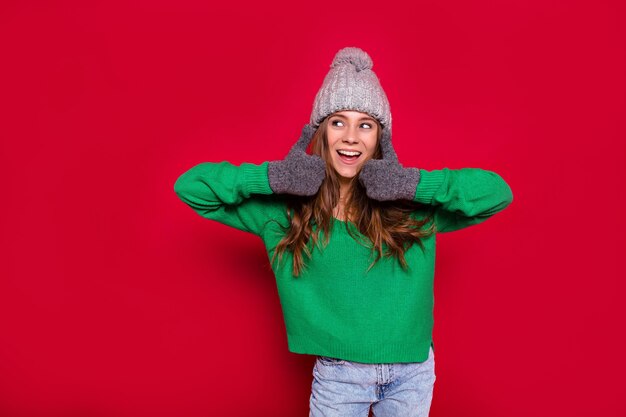 緑のセーターと冬の帽子を身に着けて新年を祝い、勝利の兆候を示す愛らしい若い女性の居心地の良い冬の休日の時間の肖像画。