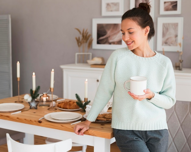 Donna accogliente appoggiata sul tavolo della cucina e tenendo la tazza