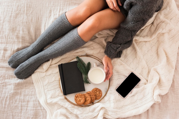 Cozy woman sitting on bed with milk, cookies and agenda