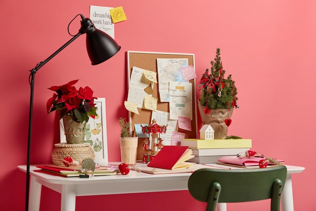 人のいない居心地の良い作業スペース。メモ帳、ランプ、来たる休日を象徴する小さな装飾されたクリスマスのモミと白い机