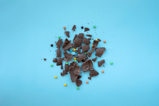 Cracked chocolate with small candies on blue table