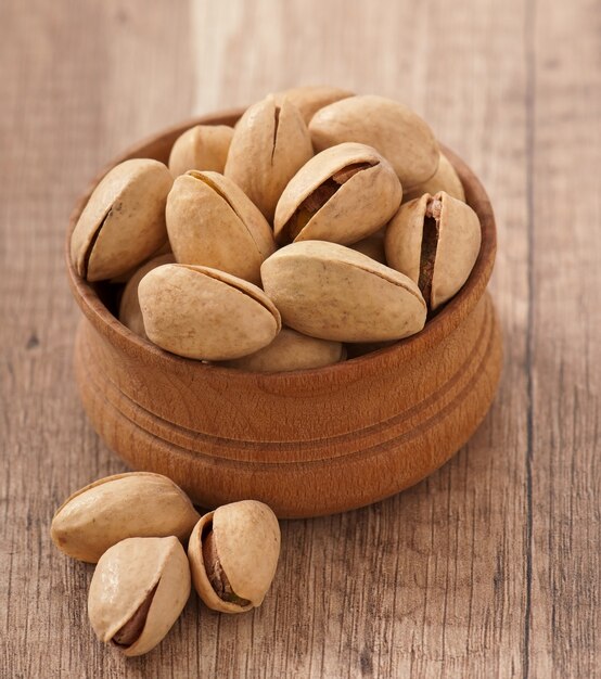 Cracked and dried pistachio nuts in a wooden bowl