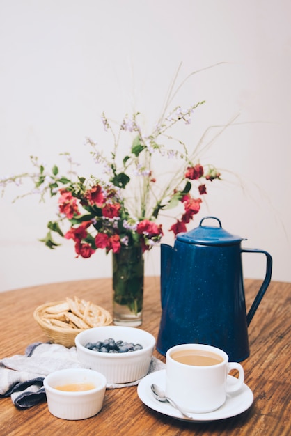 Cracker; mirtilli; inceppamento e tazza di caffè sulla tavola di legno su sfondo bianco