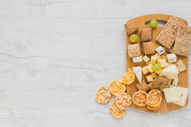 Free photo cracker, cheese blocks, grapes and crisp bread and cookies on chopping board over the desk