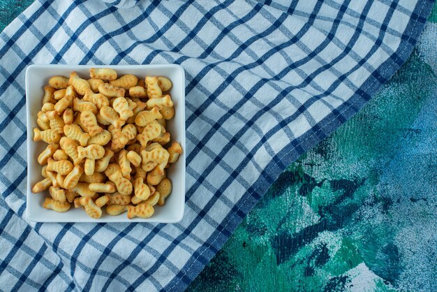 Cracker fish in bowl on tea towel on blue. 