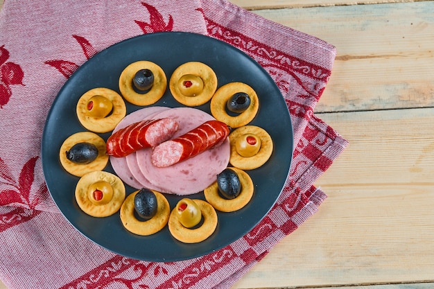 Cracker rings and slices of sausages with olives on a ceramic plate with pink tablecloth.