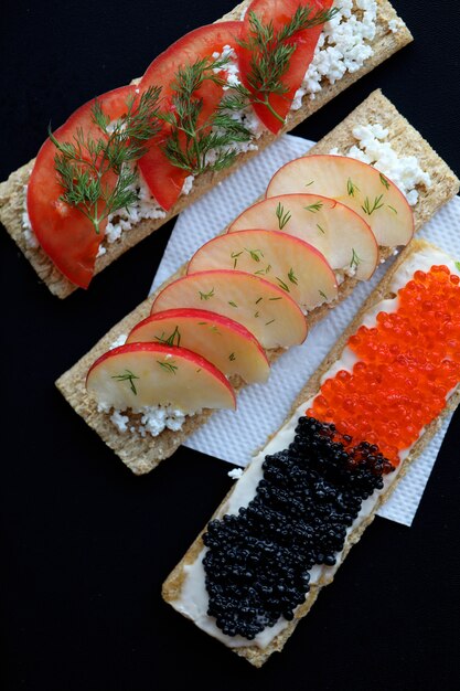 Cracker with caviar, tomatoes and sliced apples.