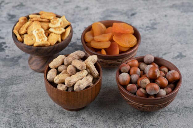 Crackers, dried apricots, hazelnuts and peanuts in wooden bowls.