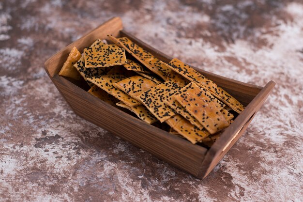 Crackers with black cumin on them in wooden tray on marble.