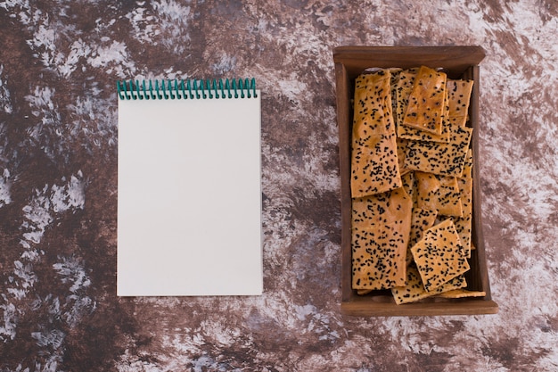 Crackers with black cumin on them in wooden tray with a notebook aside.