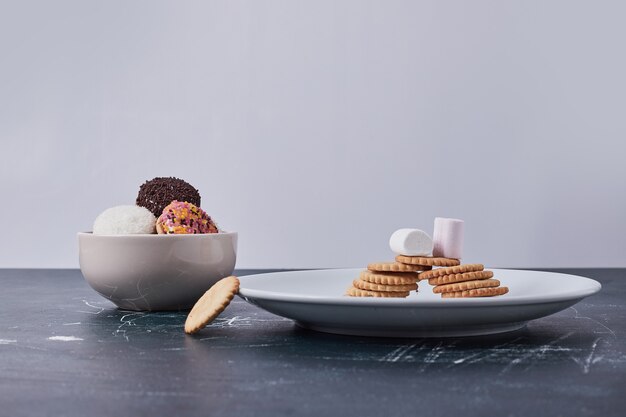 Crackers with marshmallow cookies in white dishes on blue.