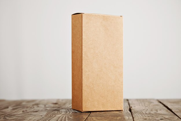 Коробка из крафт-картона, представленная вертикально на подчеркнутом матовом деревянном столе, изолированном на белом фоне
