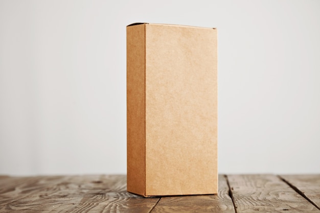 Craft cardboard package box presented vertically on stressed brushed wooden table, isolated on white background