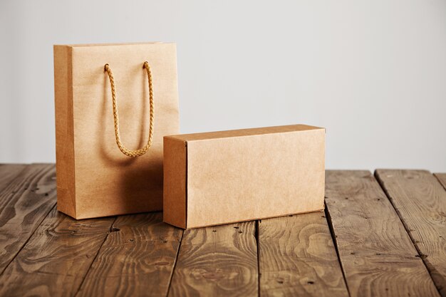 Craft paper bag and cardboard blank box presented on rustic wooden table, isolated on white background