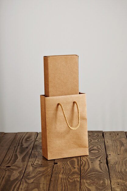 Craft paper bag with cardboard blank box inside presented on rustic wooden table, isolated on white background