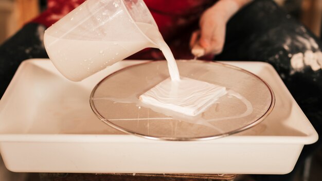 Craftswoman pouring the paint with mug on small tile over the net