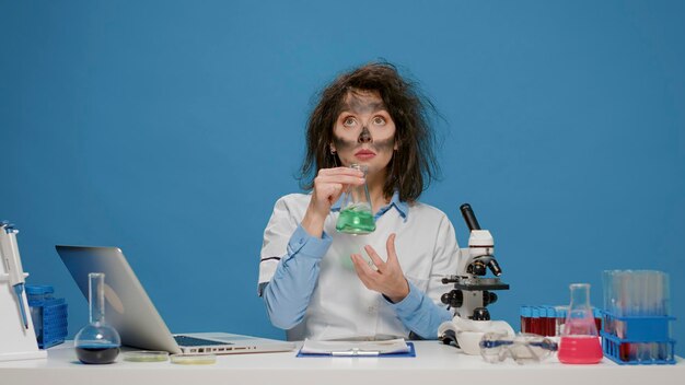 Foto gratuita chimico pazzo e divertente che analizza il bicchiere di laboratorio e si comporta da pazzo, è sciocco e fa espressioni facciali giocose sciocche. scienziato sciocco pazzo con la faccia sporca e capelli strani e stravaganti.