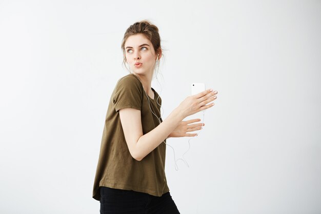 Crazy cheerful young woman dancing singing listening music in headphones over white background.