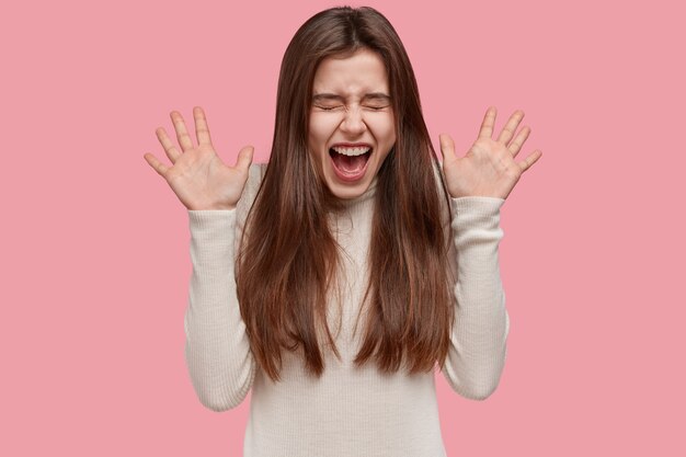 Crazy European woman shouts loudly, spreads hands, opens mouth widely, feels mad