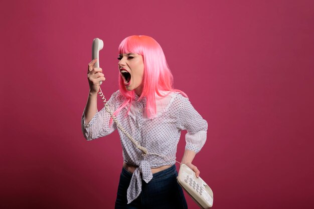 Crazy funky person screaming at landline phone call on camera, posing and talking on retro vintage telephone. Having remote conversation with stationary cord phone, trendy woman in studio.