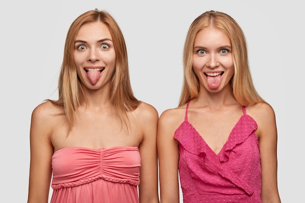 Free photo crazy happy caucasian women with blonde hair stick tongues, have funny facial expressions, dressed in fashionable clothes