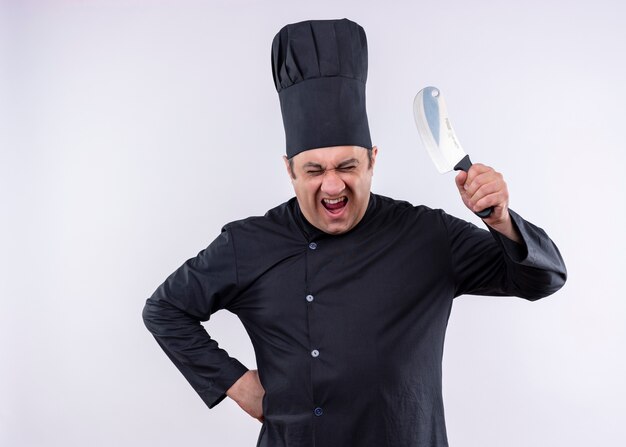 黒の制服を着て、白い背景の上に立っている怒っている顔で叫んでナイフを振る料理人の狂った男性シェフの料理人