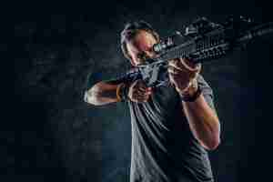 Free photo crazy middle-aged man dressed in casual clothes holding an assault rifle and aims at the target. studio photo against a dark textured wall