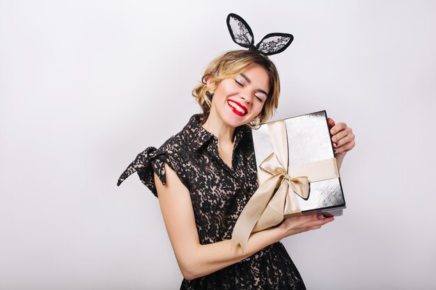 Crazy party time of beautiful women in elegant black dress with gift box celebrating birthday, having fun, dancing. Emotion face, red lips, eyes closed.