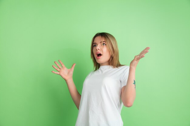 미친 충격. 녹색 벽에 고립 된 백인 젊은 여자의 초상화. 흰 셔츠에 아름 다운 여성 모델입니다.