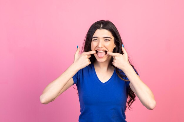 Crazy young girl stretching her mouth with her fingers and stand on pink background