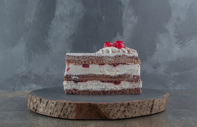 Cream and cherry topped cake slice on a board 