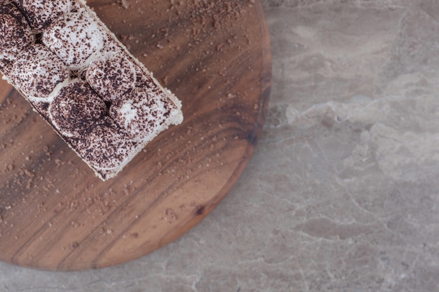 Cream and cocoa powder topped cake slice on a board on marble