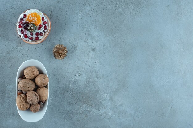 Cream and fruit topped cake and a bowl of assorted nuts on marble surface