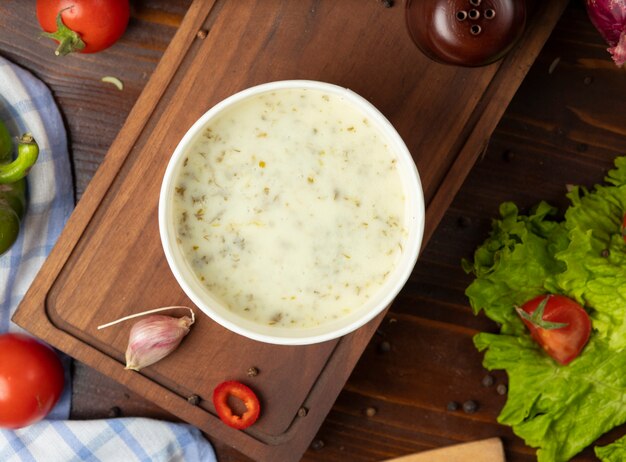 Cream mushroom soup in disposable cup bowl served with green vegetables.